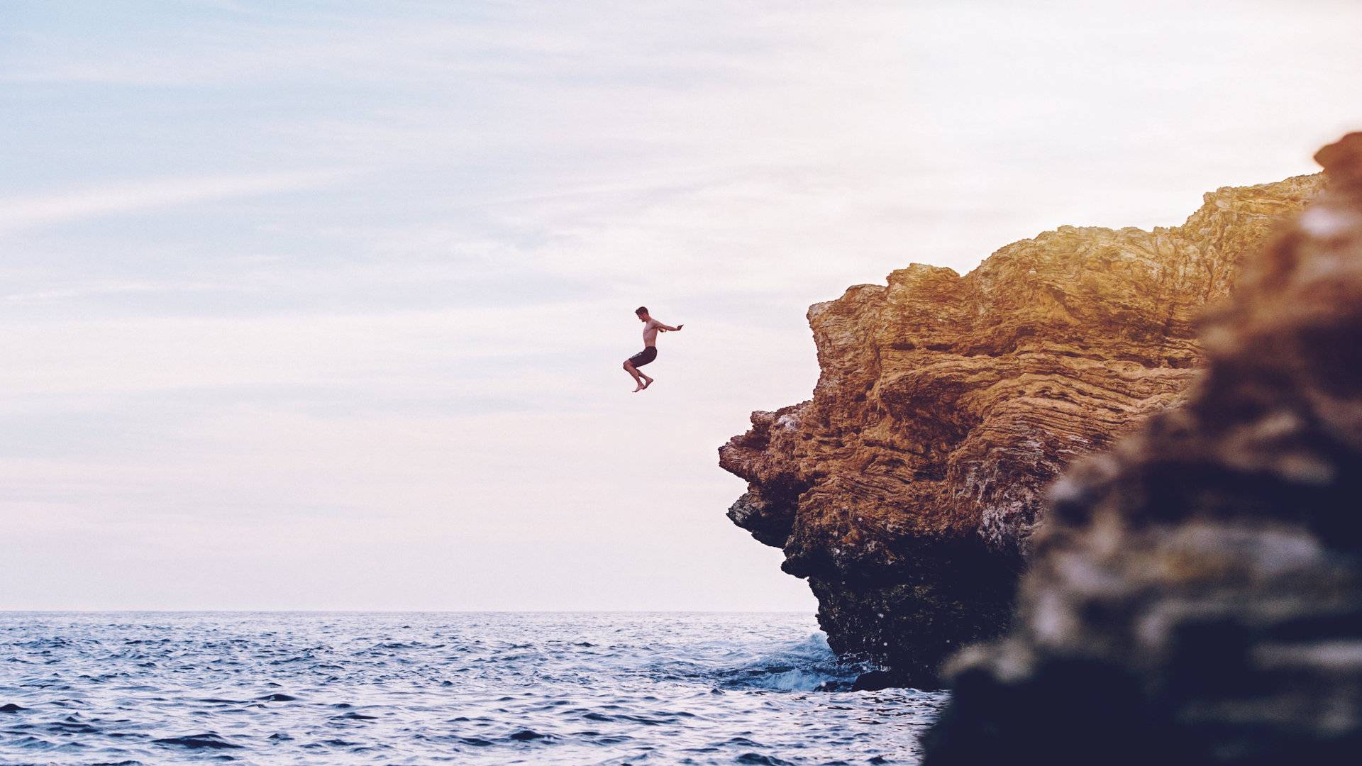 Man jumping into sea off a high cliff rock
