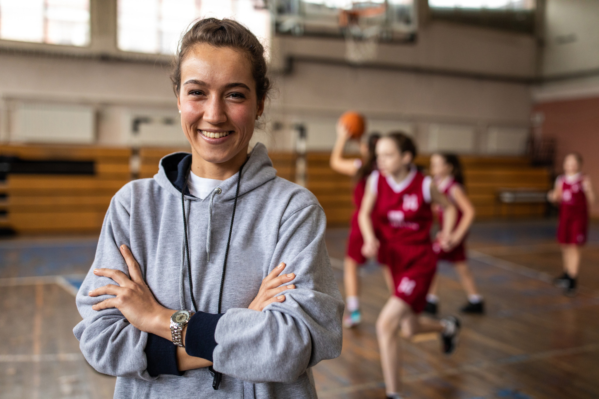 sports camp insurance, female coach smiles as basketball sports camp is practicing behind her