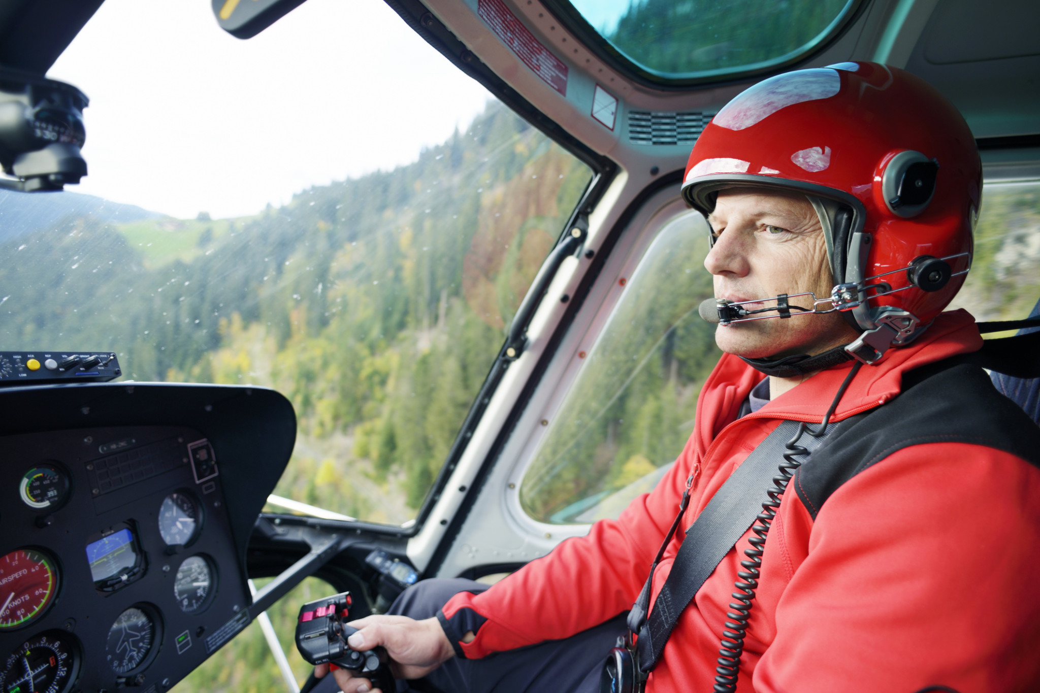 aviation insurance | A male helicopter pilot concentrates on flying his aircraft in the Swiss mountains.
