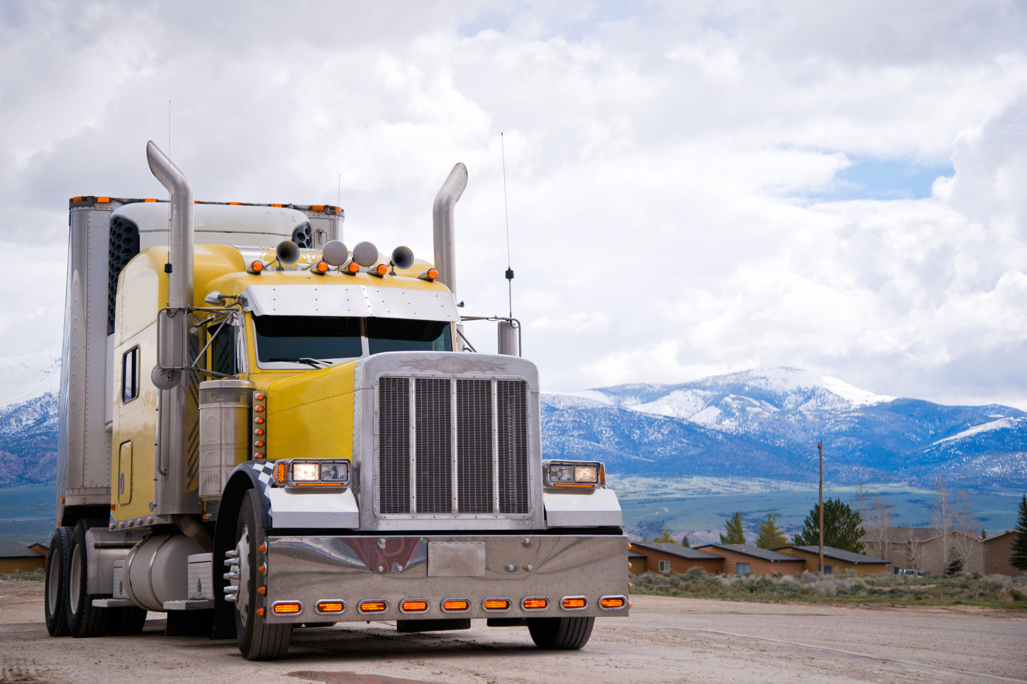 Trucking Company Insurance | Yellow big rig semi truck on rural road against mountain backdrop