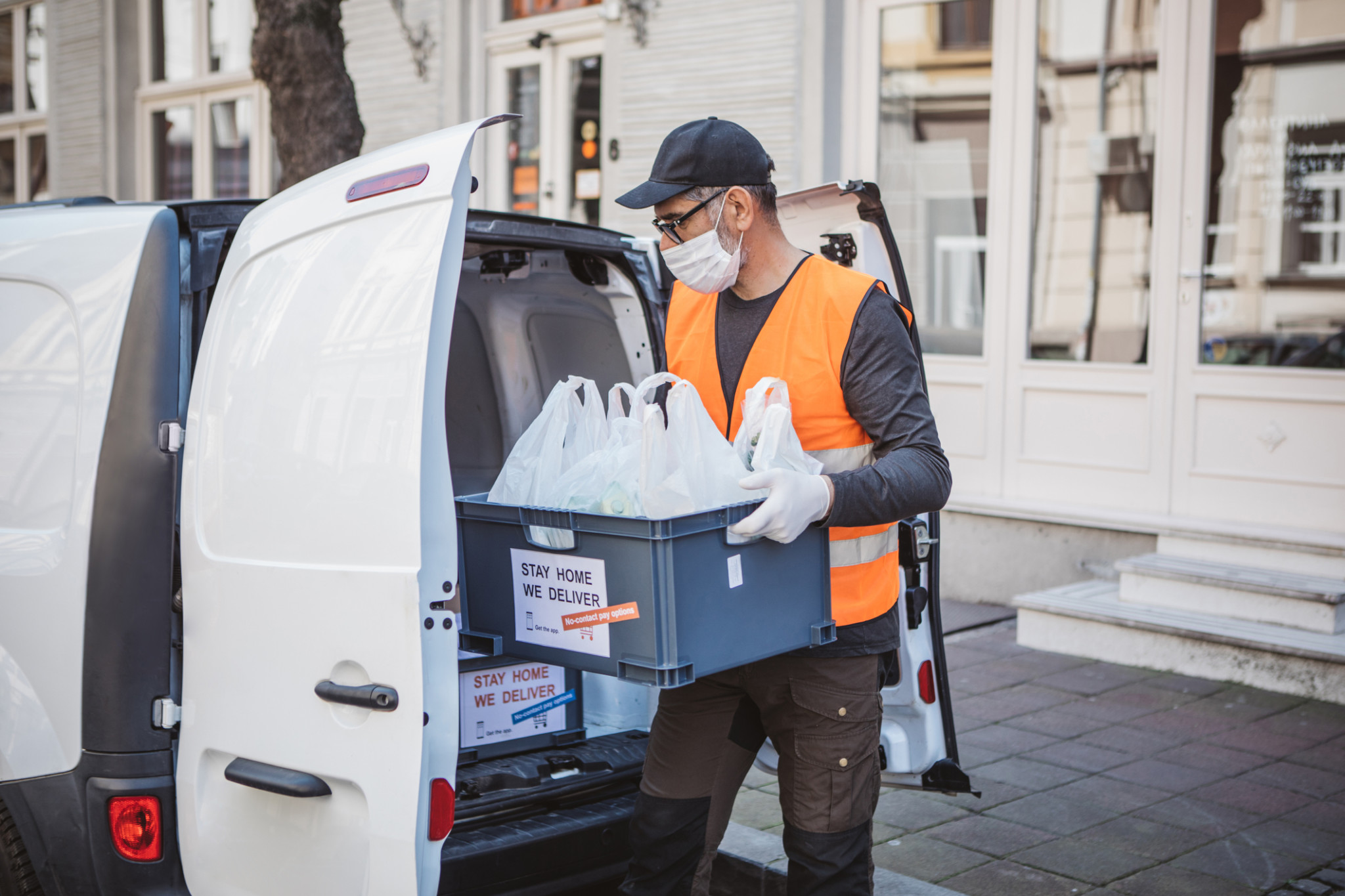 man wearing orange vest, mask and gloves putting delivery box into back of van